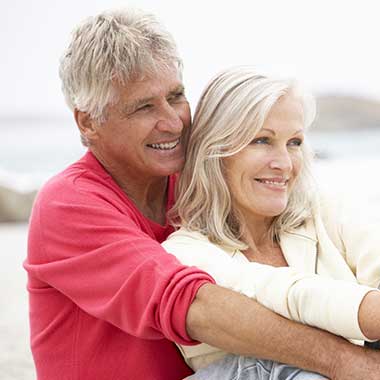 An elderly couple embracing on a beach with clear skies.